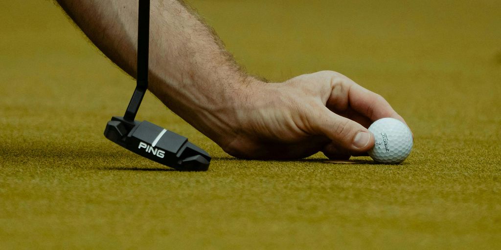 A hand is setting up to putt a golf ball.